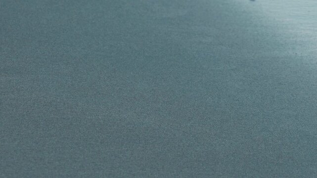 Close-Up of Gentle Waves Washing Ashore on a Dark Blue Sandy Beach, Water Seeping into the Sand