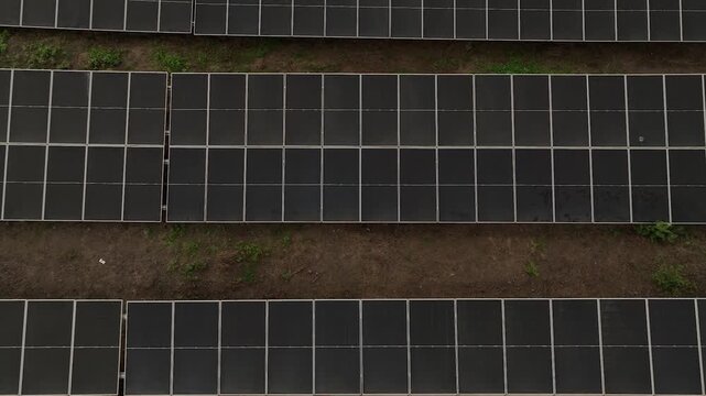 Top down straight vertical aerial view of parallel photovoltaic solar panel rows on brown dirt.