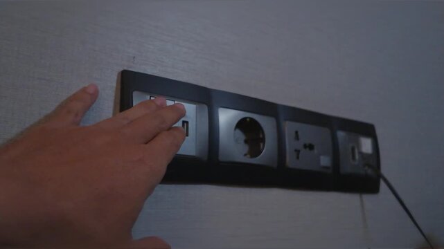 Male hand reaching towards a modern multi socket electrical outlet panel on the wall.