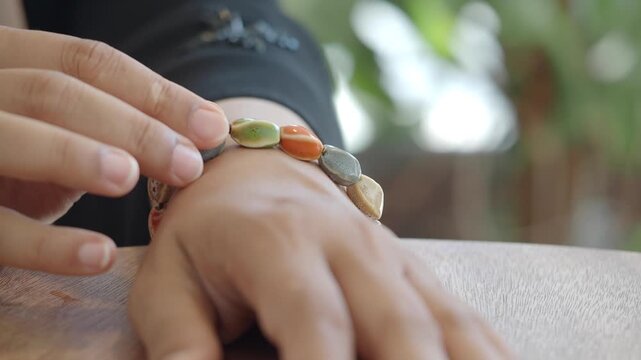 Woman hands touching colorful stone bracelet on wooden table surface during sunny daylight.
