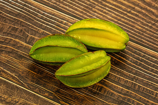 Dark wood surface with three green star fruits showing yellow flesh and brown edges, tropical fruit