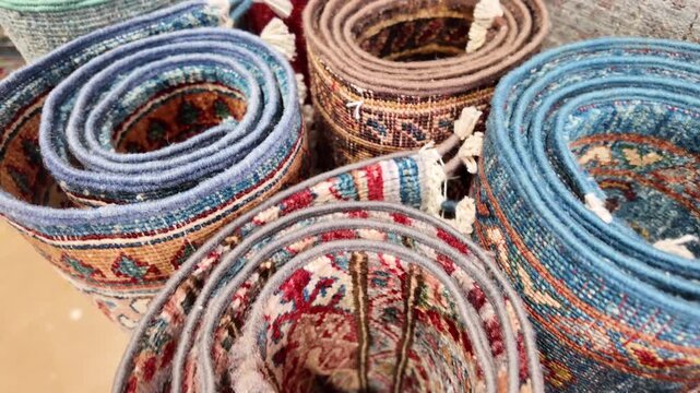 Oriental hand knotted wool rugs displayed in rolls showing intricate patterns and colors.