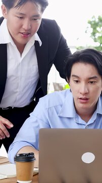 Two Asian Business Colleagues Collaborating and Discussing Work on Laptop in Office