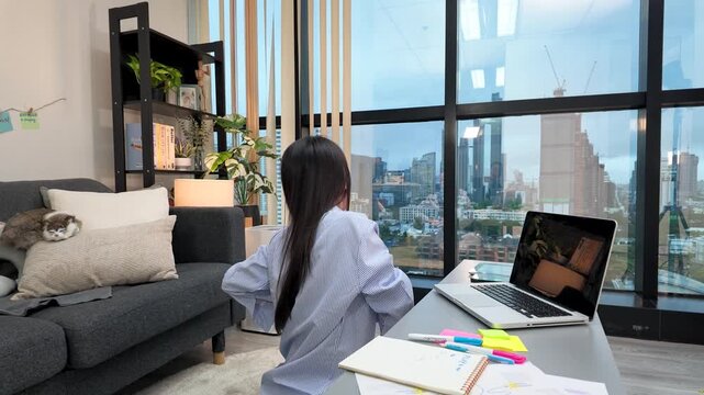 Asian Woman Stretching While Working on Laptop in Modern High-Rise Apartment