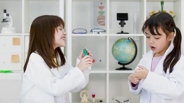 Two Schoolgirls in Lab Coats Blowing Up Balloons in Science Classroom