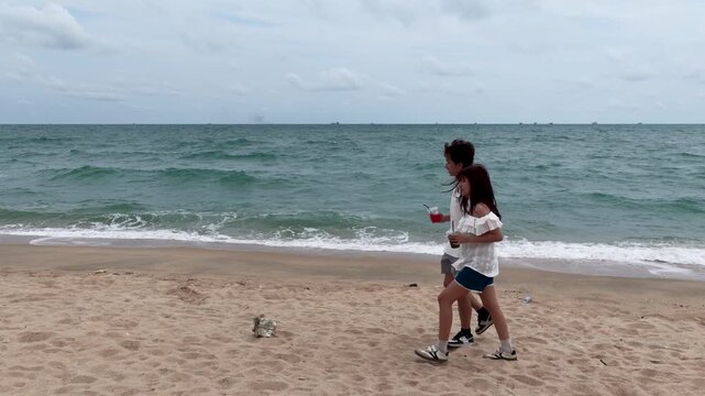 Young Asian Couple Walking and Holding Hands Along Sandy Ocean Beach