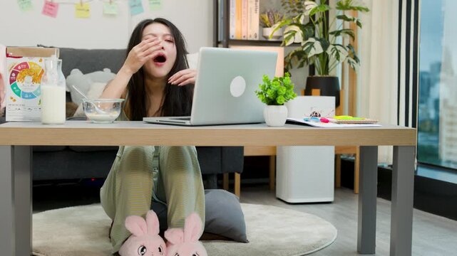 Tired Asian Woman Yawning While Working From Home on Laptop