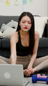 Asian Woman Stretching on Floor Following Online Workout on Laptop at Home