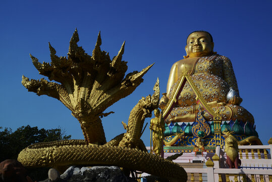 A large brilliantly gold-colored statue of Phra Maha Kaccayana Thera, holding a holy water vessel representing the 76 provinces standing 20 meters at Wat Lang San Prasit.