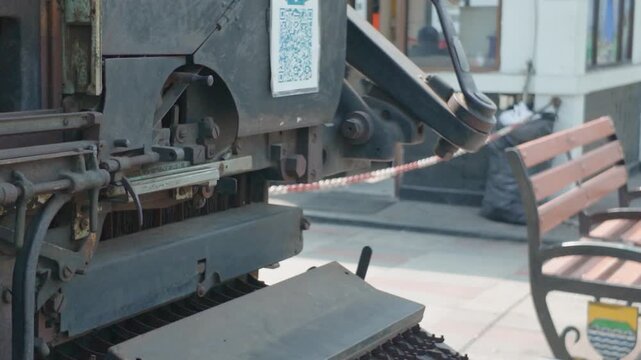 Vintage antique mechanical printing machine displayed outdoors on a paved terrace.