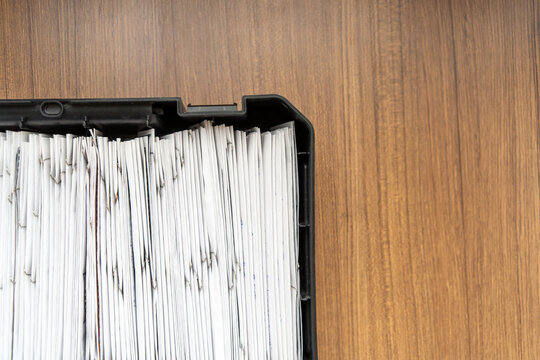 Thick stack of paper documents in black storage tray on wooden tabletop. Paper archive and record keeping. Office filing and document storage. Administrative paperwork, business records