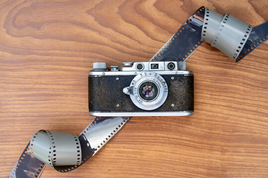 Vintage film camera with curling photographic film on wooden tabletop. Analog photography and classic camera equipment. Film development, image making and visual storytelling.