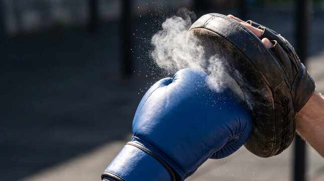 Blue boxing glove striking a padded mitt, creating a cloud of dust and impact, symbolizing combat sports training and power