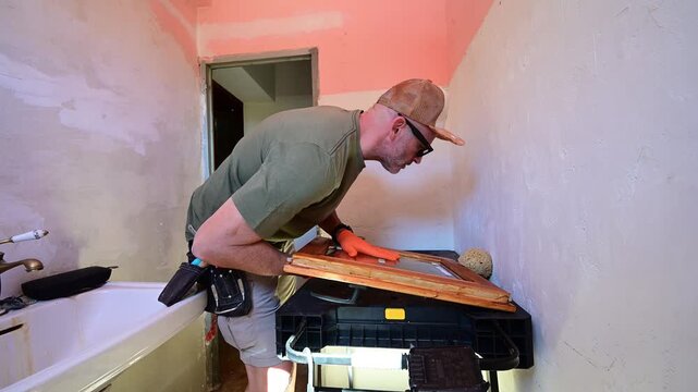 Handyman sanding a wooden window frame during bathroom renovation
