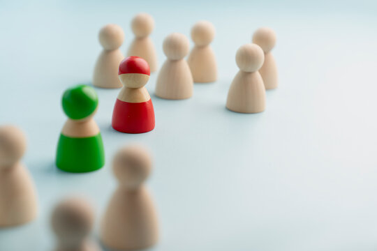 Leadership competition and corporate partnership concept, red and green wooden peg dolls standing ahead of crowd on blue background, symbolizing strategic guidance, choice, and talent.