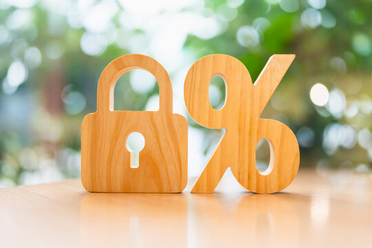 Locked interest rate and financial security concept, wooden padlock standing beside wooden percentage symbol on table, representing fixed mortgage rate, protected savings, and loan guarantee.
