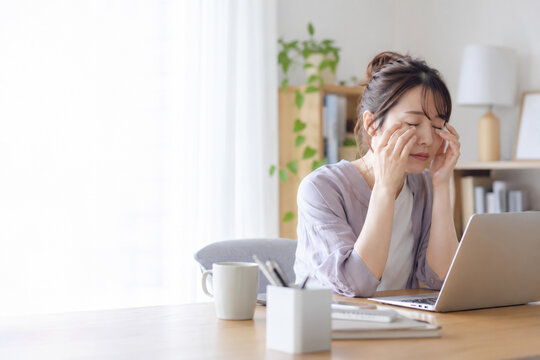 自宅でパソコン作業中に目をこすって疲れを感じる女性