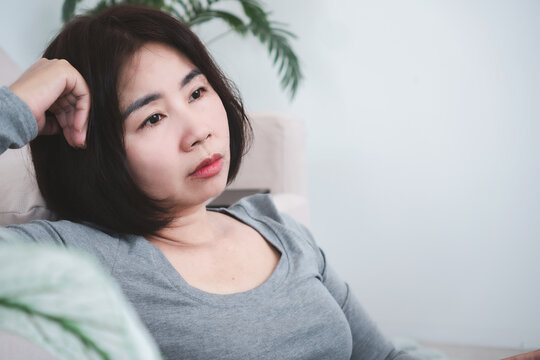 Depressed Asian woman leaning on sofa feeling sad, lonely, tired, suffering from burnout, mental stress, anxiety disorder, thoughtful melancholic mood, emotional problem, depression concept