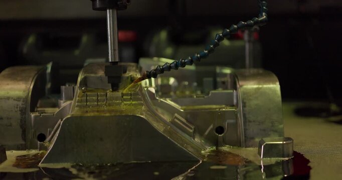 Milling machine cutting a large steel mould with cutting fluid flowing in a machining shop