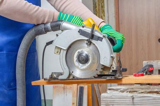 Gloved worker operating a circular saw over a wooden plank in a workshop. Wood cutting and carpentry. Power tool safety and workshop craftsmanship. DIY woodworking and home repair