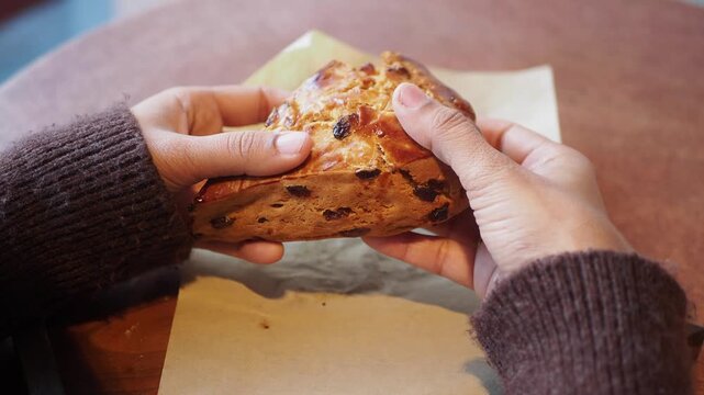 Hands holding delicious triangular cranberry scone in cozy cafe setting with warm lighting.