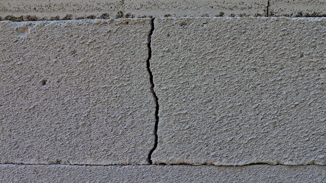 Cracked concrete wall texture with vertical fissure on grey block surface.
