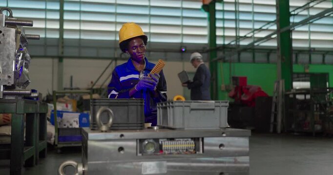 African woman technician inspecting a yellow coil die spring beside a large steel mould