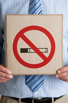 Man in striped shirt and tie holding handmade cardboard sign with no smoking symbol, public health warning and non smoking policy awareness concept
