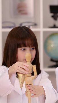 Asian Schoolgirl in Lab Coat Examining Wooden Mannequin in Science Classroom