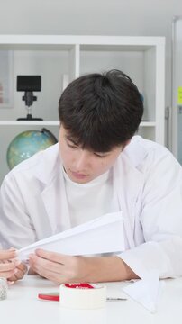 Teenage Student in Lab Coat Folding Paper Airplane in Science Classroom