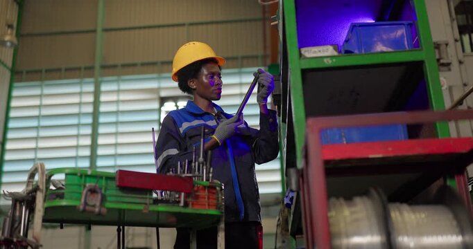 African woman technician checking ejector pins at a tooling storage rack in a factory tool crib