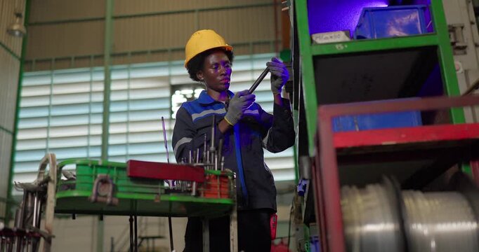 African woman technician checking ejector pins at a tooling storage rack in a factory tool crib