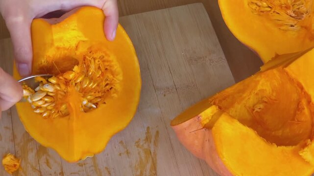 Person removing seeds from sliced pumpkin on wooden table, close up. Culinary preparation, autumn cooking recipe. Thanksgiving, Halloween.
