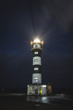 Black and white lighthouse shining under a starry night sky