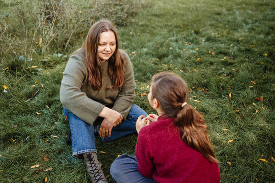 A woman talking with a child girl while sitting on green grass