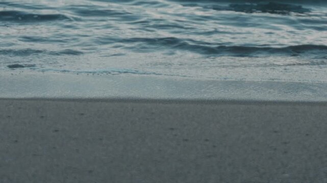 Close-Up of Small Waves Lapping Against a Blue-Gray Sandy Beach