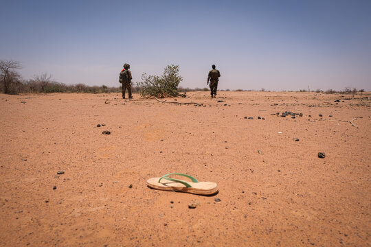 Single sandal lying in the sand with two French soldiers beyond in the Sahel near Tin-Akoff, Burkina Faso