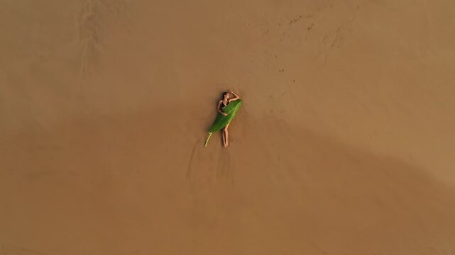 Woman Lying on Sandy Beach Under a Large Banana Leaf Top View