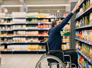 Obraz premium Man Using Wheelchair Reaching for Product on Supermarket Shelf, Independent and Accessible Shopping