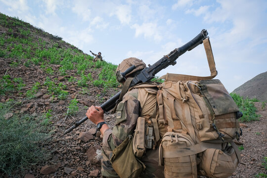 Soldier carrying a support weapon uphill during French Army officer cadet desert combat training in Djibouti