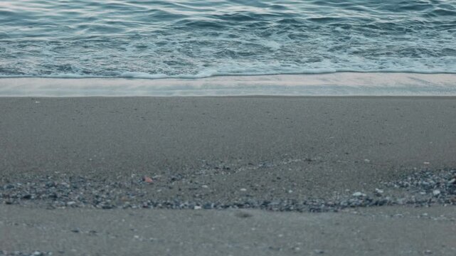 Close-Up of Small Waves Lapping Against a Blue-Gray Sandy Beach