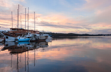 Traditional wooden sailing ships moored in calm harbor at sunrise with colorful reflections, Croatia © Sonja