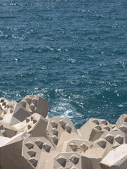 Fototapeta premium Concrete Tetrapod Breakwater Blocks Along Deep Blue Sea Coastline