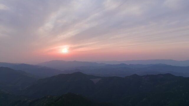 Early morning sun rises low on horizon in mountain landscape at dawn - aerial view