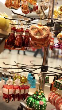 Vertical screen colorful Christmas ornaments shaped like festive food and drinks hang on store display creating cheerful holiday shopping mood with playful seasonal decor