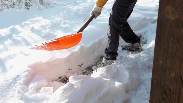 Close-up of a snow shovel clearing fresh snow outside a country house on a sunny winter day, showing the process of snow removal and winter yard maintenance.