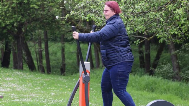 Overweight woman exercising on outdoor elliptical trainer in park