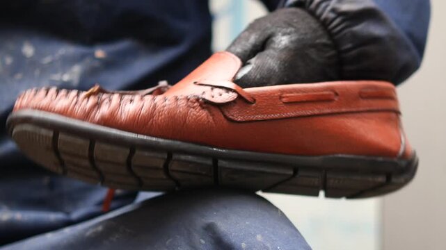 Skilled artisan polishing brown leather loafer shoe with cloth for perfect finish.