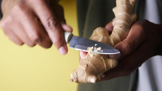 Close-up footage of hands peeling ginger root with small knife for cooking or health.