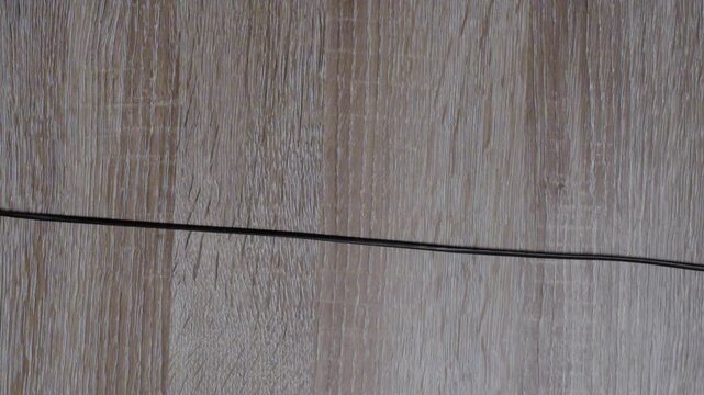 Black tape line on wooden floor, caucasian stagehand smoothing adhesive strip for set prep, closeup of hand aligning cable cover, calm focused motion, removable floor marker detail